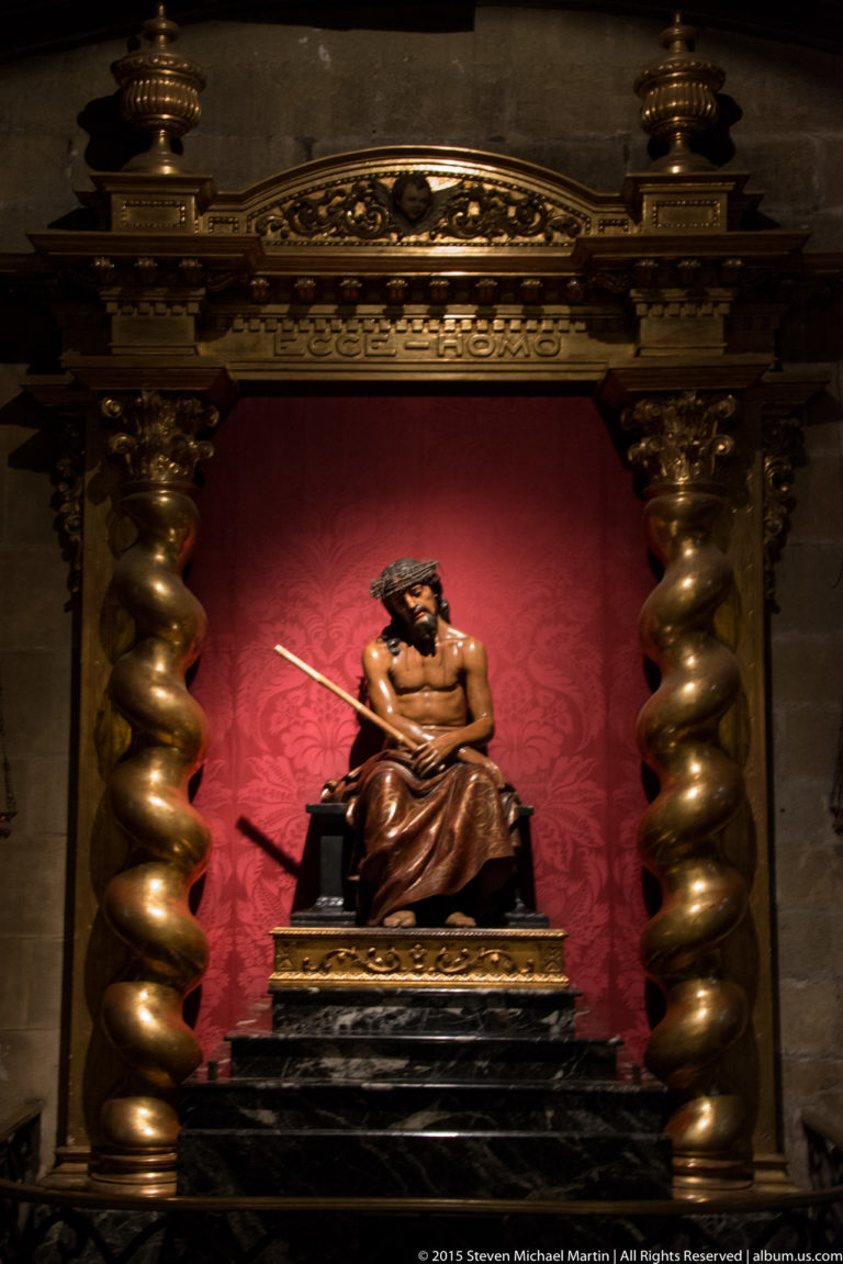 Seated polychrome religious figure in a red-backed niche framed by large twisted gilded columns.