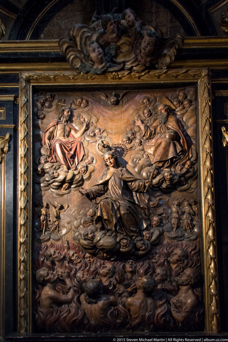 Large dark carved religious relief crowded with robed figures, clouds, and smaller figures in a dramatic narrative scene.
