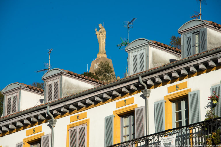 Numbered upper-story windows and tiled dormers with the distant Sacred Heart monument rising above the roofline.