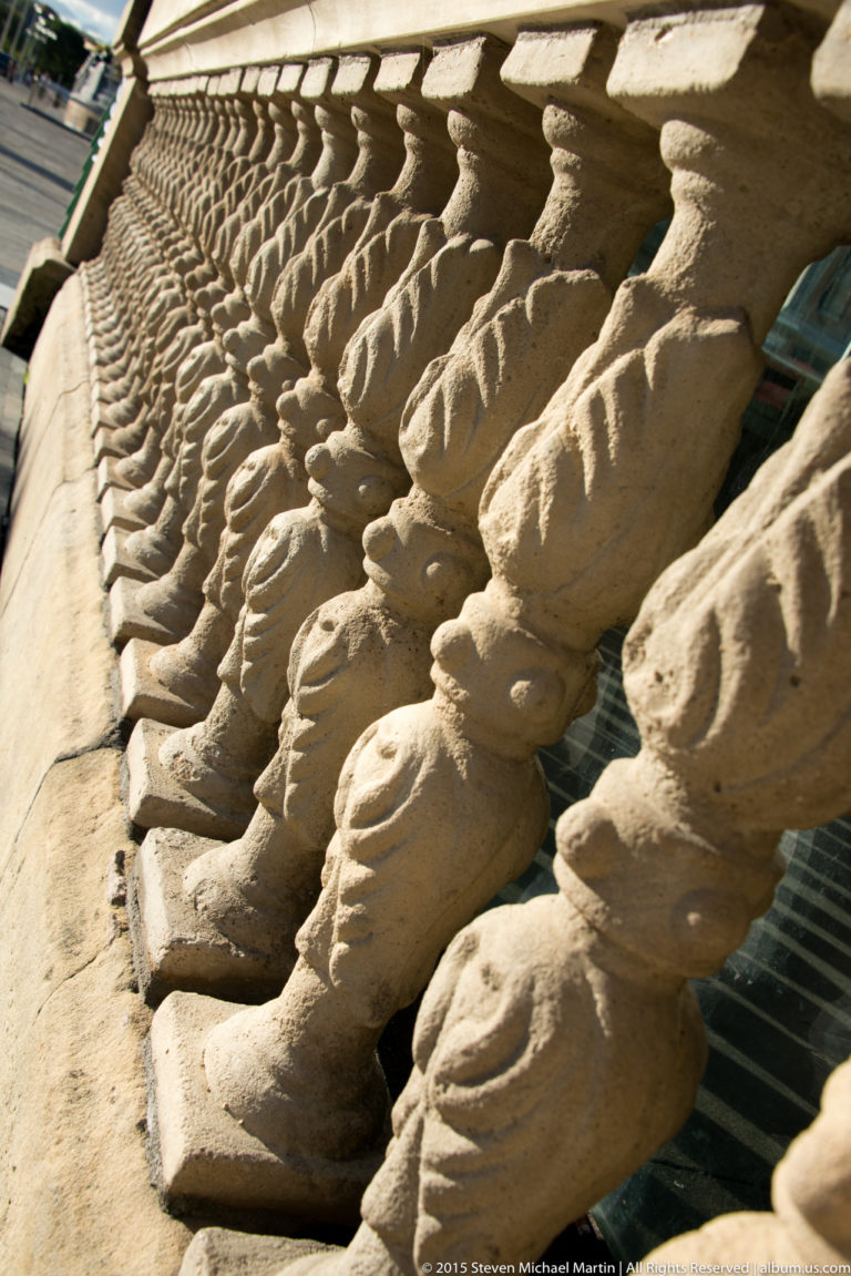 Close oblique view along a stone balustrade, with repeating carved balusters strongly lit by sunlight.