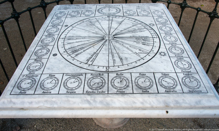 Top-down view of a stone table engraved with a large radial dial and rows of small international clock faces.