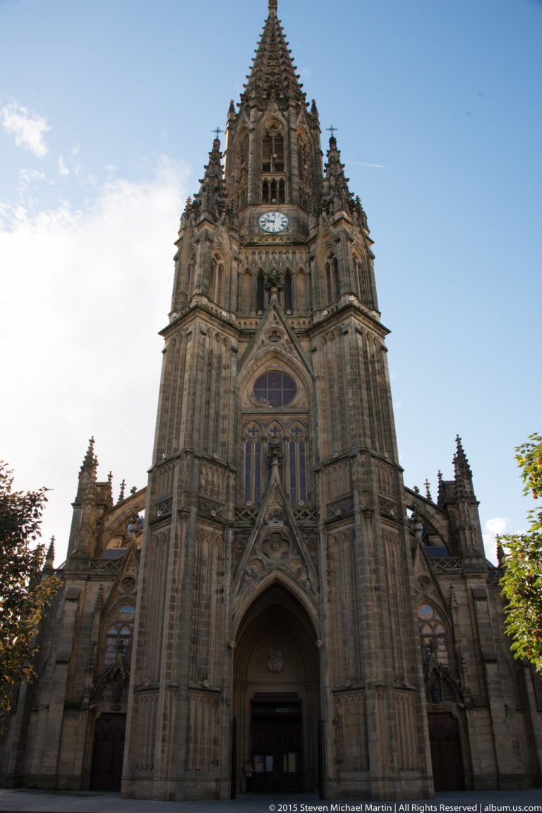 Front view of Buen Pastor Cathedral with tall Neo-Gothic central spire, clock, pointed arches, and traceried windows.