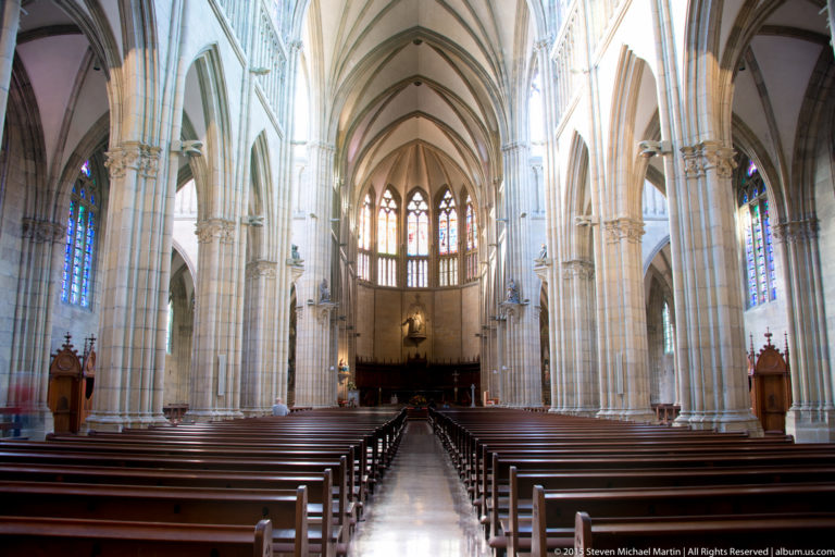 Bright Neo-Gothic nave of Buen Pastor Cathedral with wooden pews, clustered piers, pointed arches, rib vaults, and stained glass.