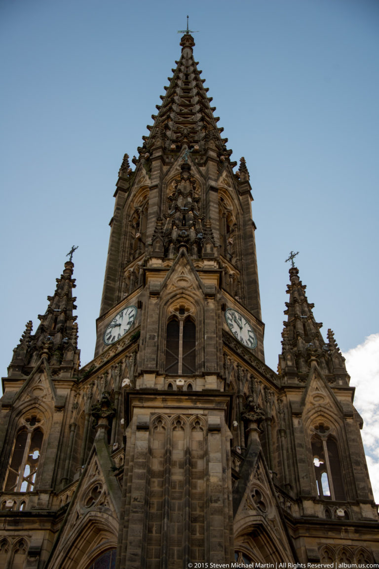 Low-angle close view of Buen Pastor Cathedral’s Neo-Gothic tower with clock faces, pointed gables, pinnacles, and carved ornament.