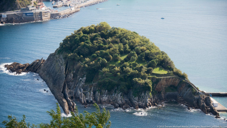 Elevated close view of wooded Santa Clara Island with steep rocky cliffs and a small shore structure in blue water.