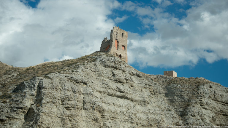 Ruined rectangular stone tower standing alone on the crest of a steep eroded ridge beneath dramatic clouds.