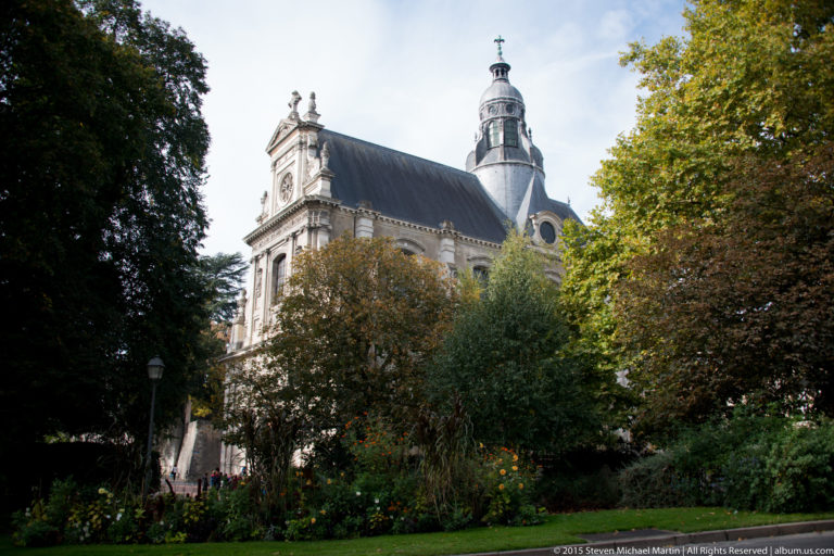 Historic church with steep roof and tower partly screened by trees and garden plantings in Blois.