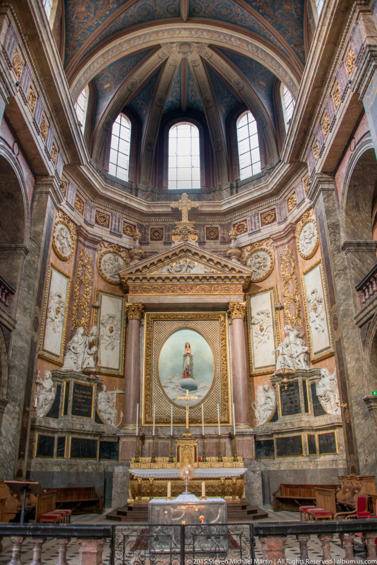 Ornate sanctuary with gilded altar, painted apse, marbleized wall panels, and decorative vaulting.