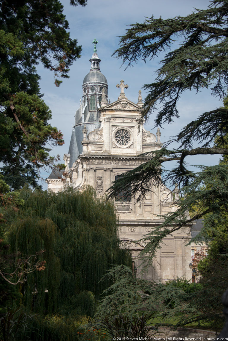 Upper façade and tower of Saint-Nicolas church in Blois framed by dark evergreen branches.