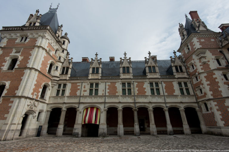 Brick-and-stone Louis XII wing of Blois château with arcaded ground floor, dormers, and corner towers.