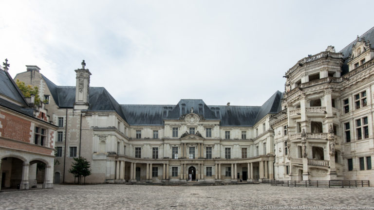 Wide courtyard view of Blois château showing classical, Renaissance, and brick-and-stone wings around the open court.