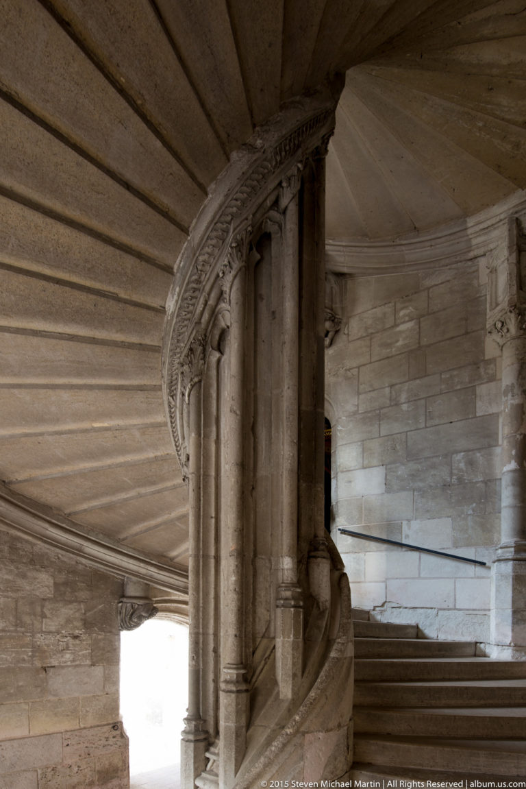 Interior stone spiral staircase curving upward around a central support inside Blois château.