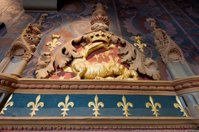 Gilded crowned salamander above a row of fleurs-de-lis within ornate painted decoration at Blois château.