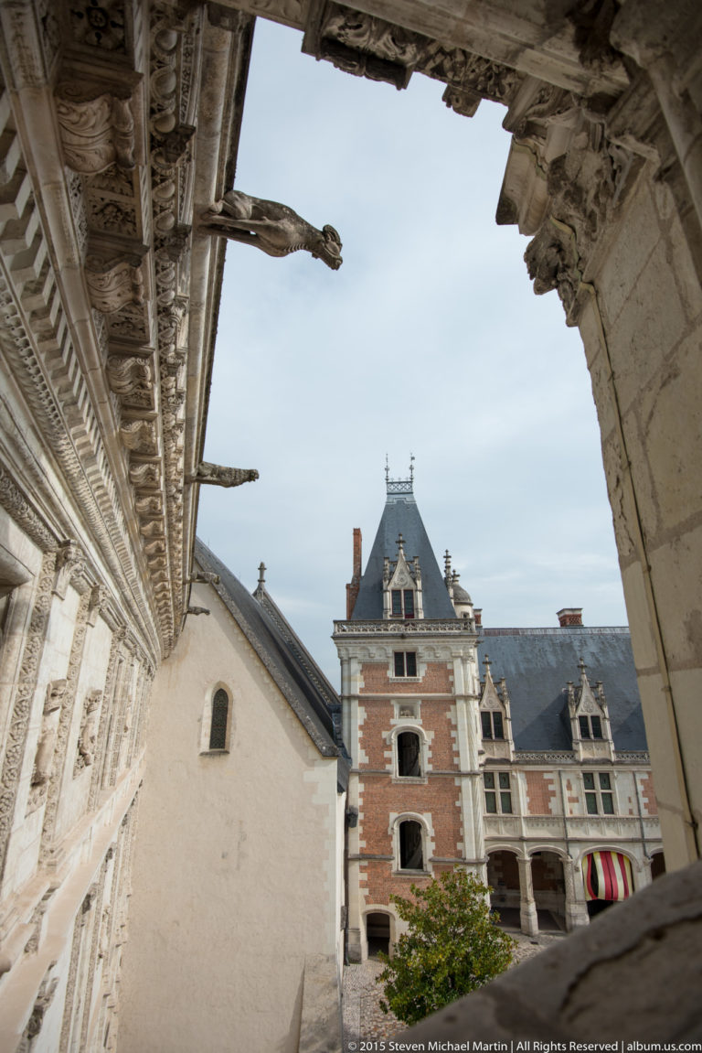 Blois château courtyard seen through a carved stone arcade toward the brick-and-stone Louis XII wing.
