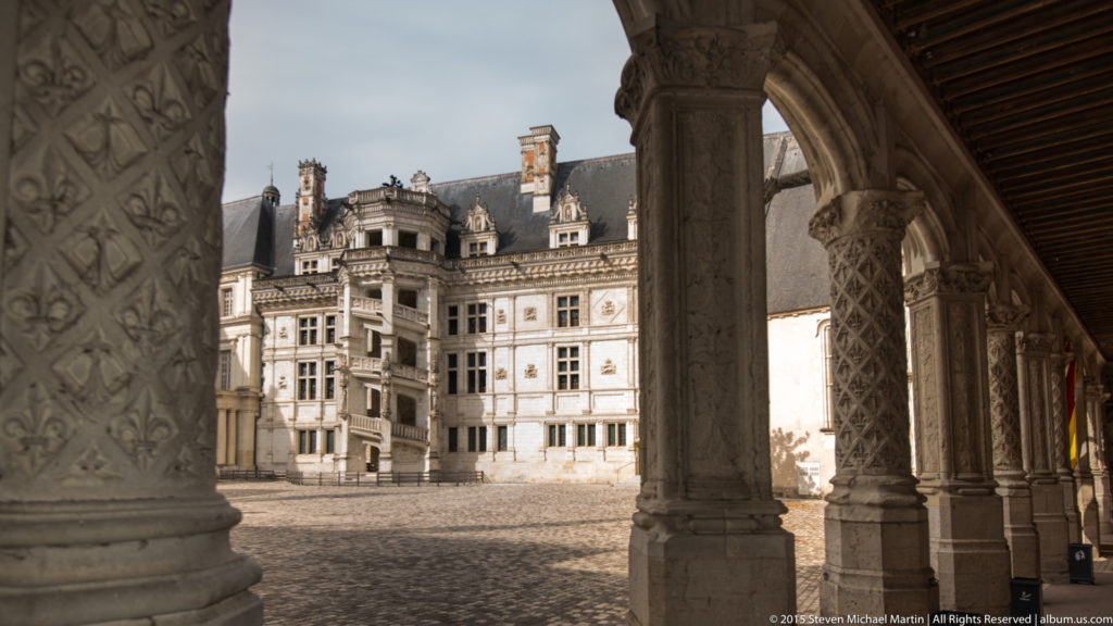 Renaissance façade of Blois château seen across the courtyard through carved stone columns and arches.