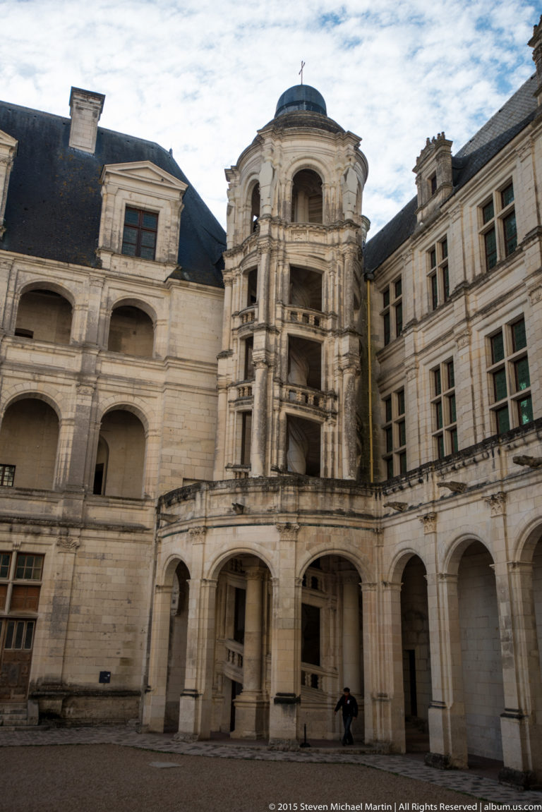 Inner courtyard of Château de Chambord with arcades, carved limestone façades, dormers, and a projecting tower pavilion.