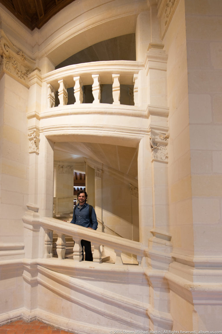 Curved pale-stone balustrade and gallery inside Château de Chambord, with carved details and a visitor behind the railing.