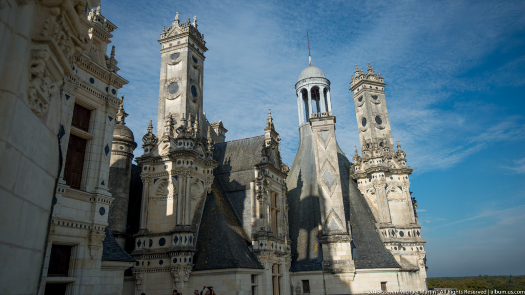 Cluster of tall chimneys, lanterns, carved stone towers, and steep slate roofs on Château de Chambord.