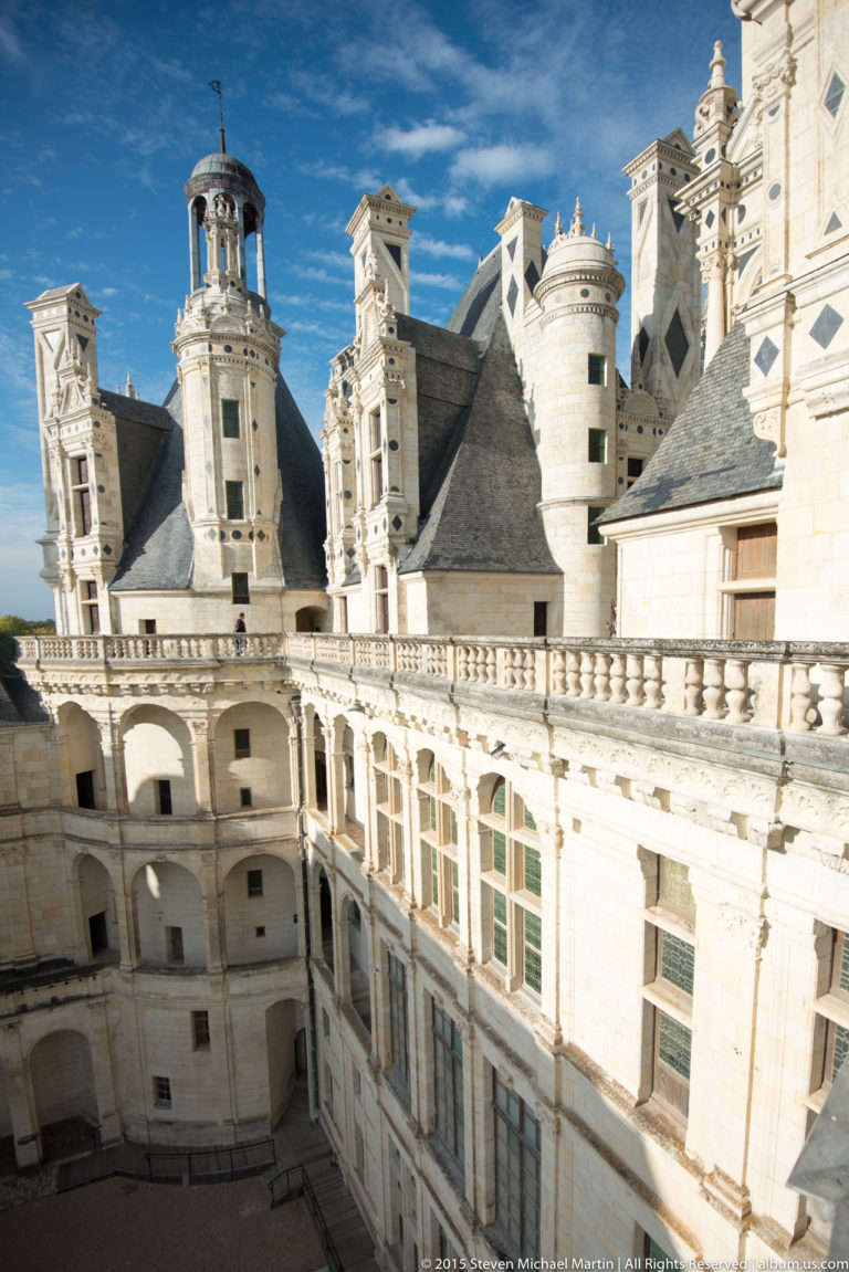 Elevated view along a balustraded Château de Chambord terrace with windows, round towers, dormers, and steep slate roofs.