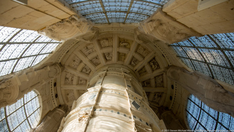 Upward view through Château de Chambord’s central double-helix staircase, with curving stone flights beneath a glazed lantern.