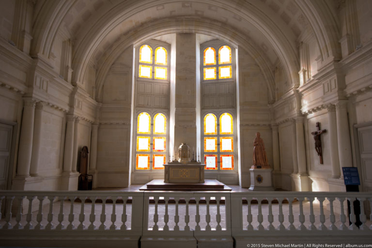 Vaulted chapel-like interior at Château de Chambord with four glowing windows, statues, central altar, and stone balustrade.