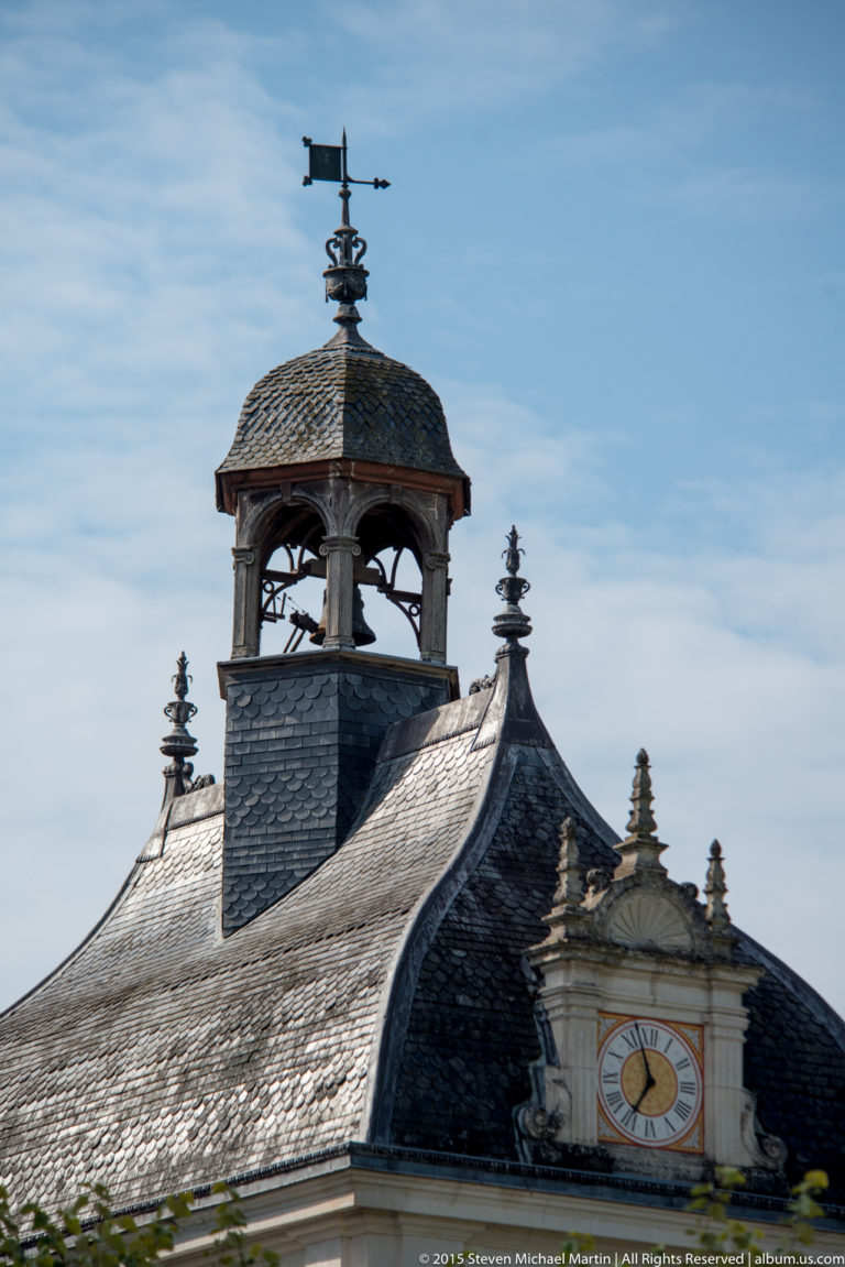 Slate roof with open lantern, weather vane, finials, and decorative clock face at Château de Chenonceau.