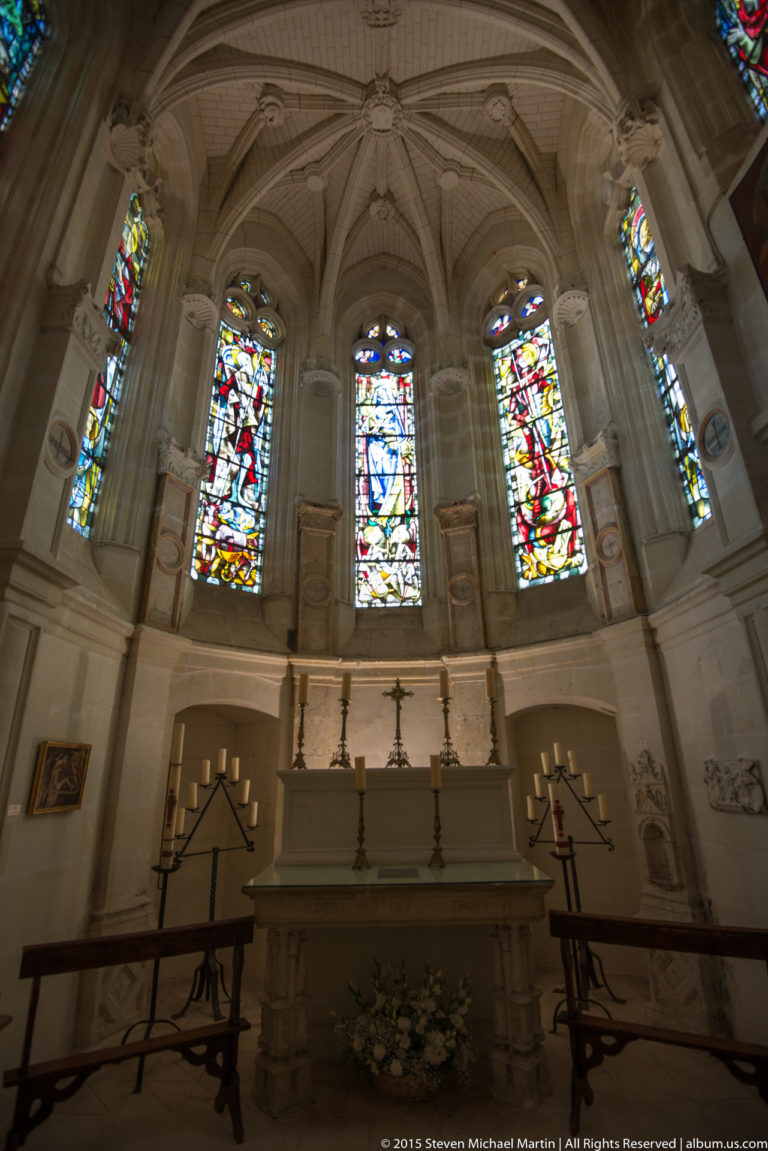Stone altar beneath tall stained-glass windows and ribbed vaulting in the chapel of Château de Chenonceau.