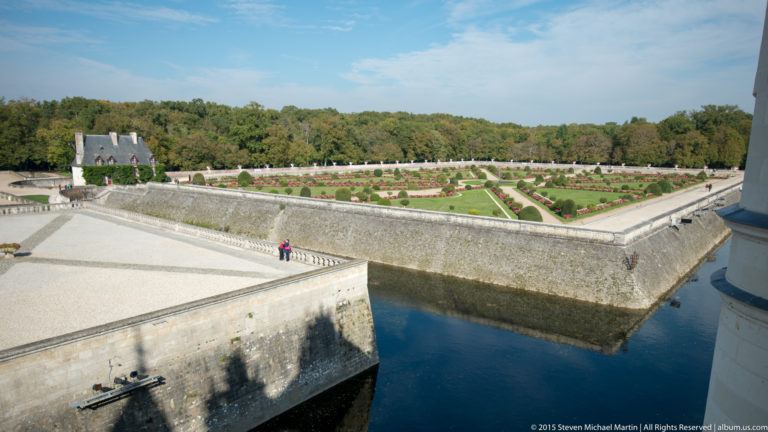 Elevated view over a geometric formal garden, stone walls, and water channel at Château de Chenonceau.