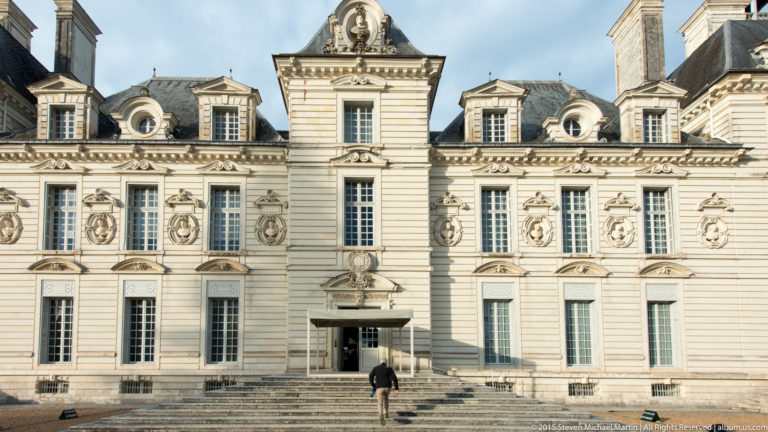 Close view of Château de Cheverny’s central entrance bay with tall windows, sculpted medallions, dormers, steps, and a visitor for scale.