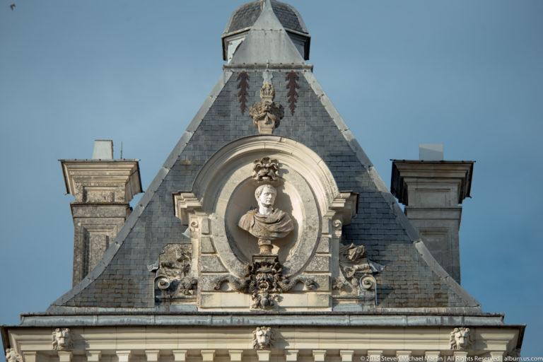 Steep slate-roofed pavilion at Château de Cheverny with a sculpted bust in an arched niche and carved ornament below.