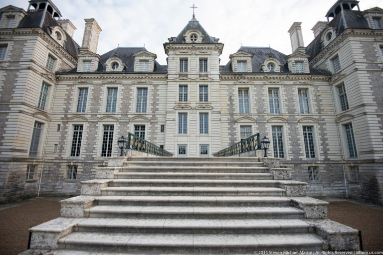Pale stone façade of Château de Cheverny above a broad staircase with iron railings, tall windows, dormers, and roof pavilions.