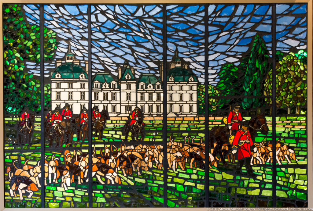 Stained-glass scene of Château de Cheverny with mounted riders and a pack of hunting hounds across a green landscape.