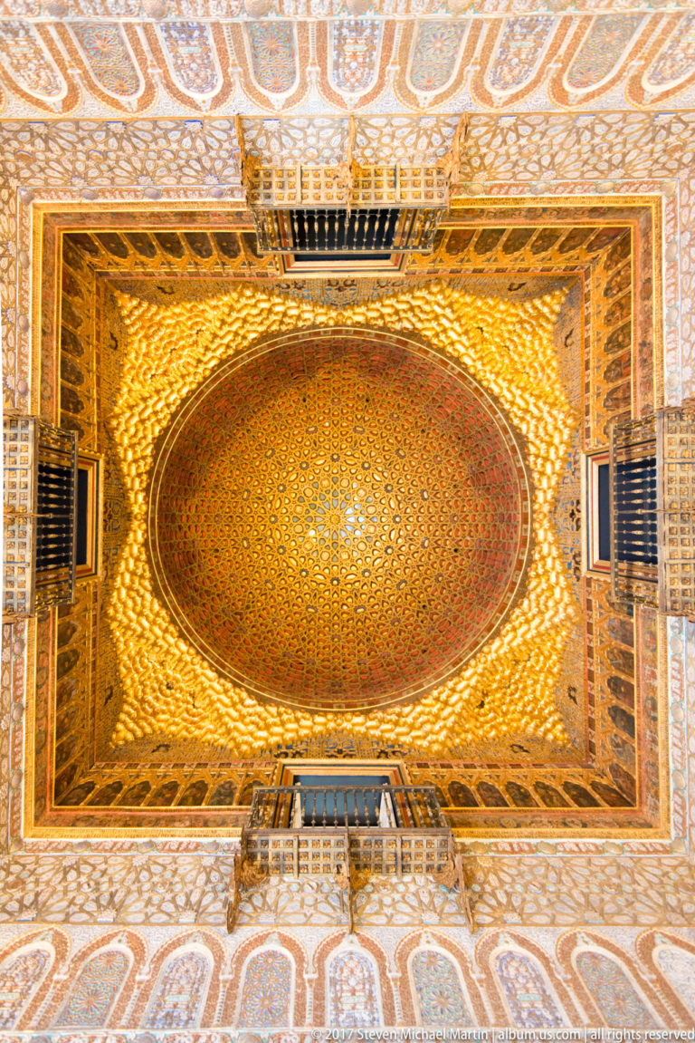 Upward view of the gilded geometric wooden dome and richly decorated ceiling framework in the Salón de Embajadores.
