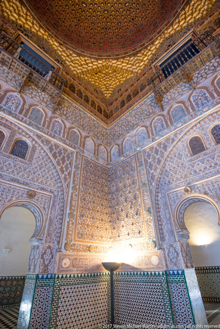 Oblique interior view of patterned plaster walls, tile dado, lattice screens, and the gilded dome in the Hall of Ambassadors.