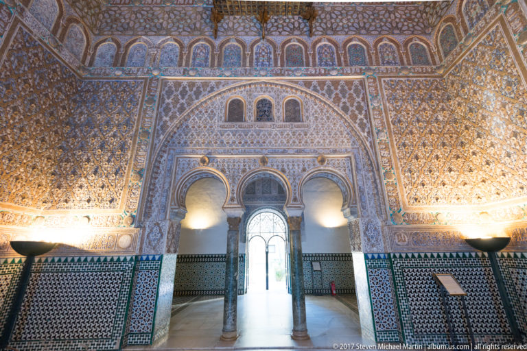 Three arched openings with slender columns, carved plaster, and geometric tile dado in the richly decorated Hall of Ambassadors.