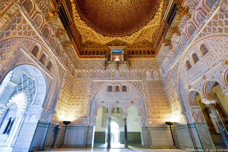 Wide interior view of the Hall of Ambassadors with tiled dado, carved plaster walls, arched openings, and gilded dome overhead.