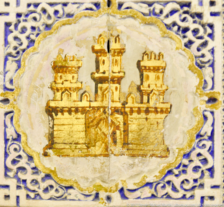 Close-up of a glazed tile medallion showing an ochre three-towered castle surrounded by cobalt-blue interlace.