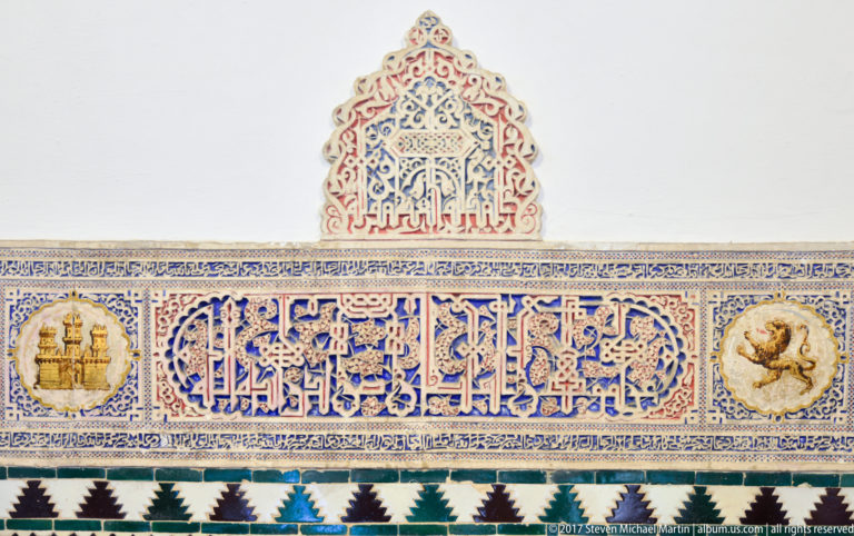 Blue Arabic calligraphy on a ceramic frieze flanked by castle and lion medallions, with geometric tile bands above and below.