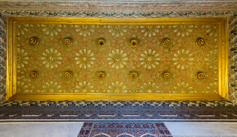 Rectangular painted wooden ceiling with green, red, cream, and gold patterns, punctuated by rows of gilded rosette-like bosses.