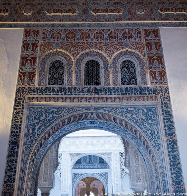 Polychrome arched doorway with geometric tilework, arabesque decoration, three upper openings, and additional arches visible beyond.