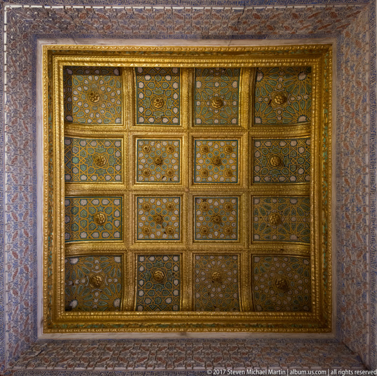 Gilded rectangular coffered ceiling divided into patterned geometric panels and enclosed by a broad decorative border.