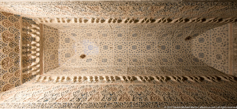 Close view of pale plaster vault covered with intricate geometric ornament and projecting rows of small faceted decorative forms.