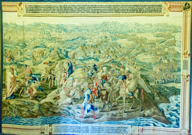 Tapestry showing mounted soldiers and horses crossing shallow water, with large troop formations extending across the distant landscape.