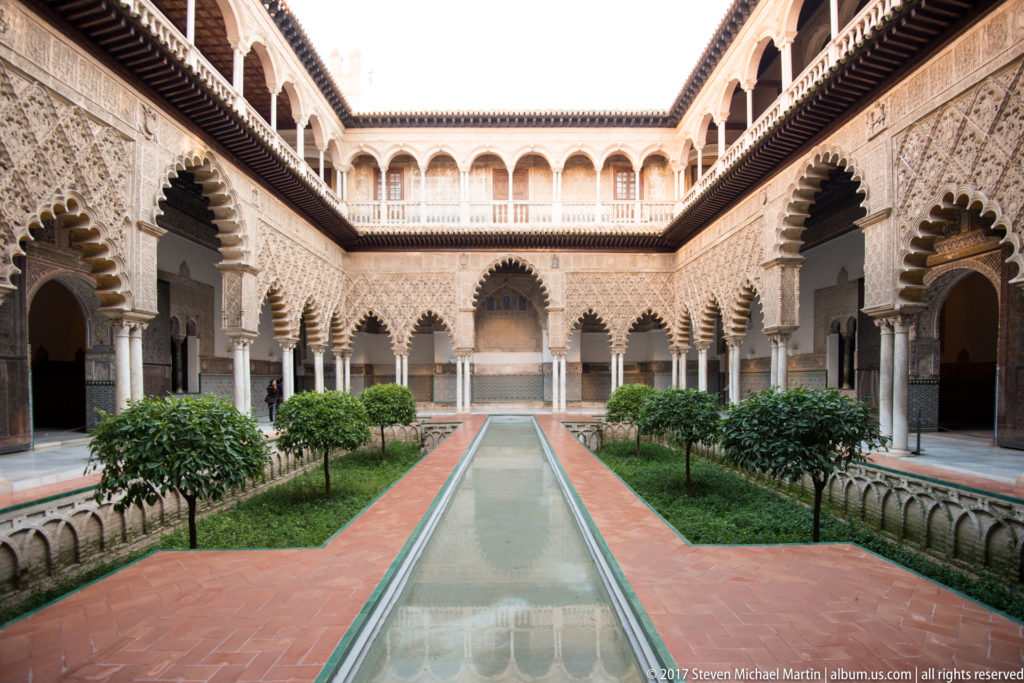 Long reflecting pool, sunken gardens, citrus trees, and ornate arcades in the Patio de las Doncellas at the Real Alcázar.