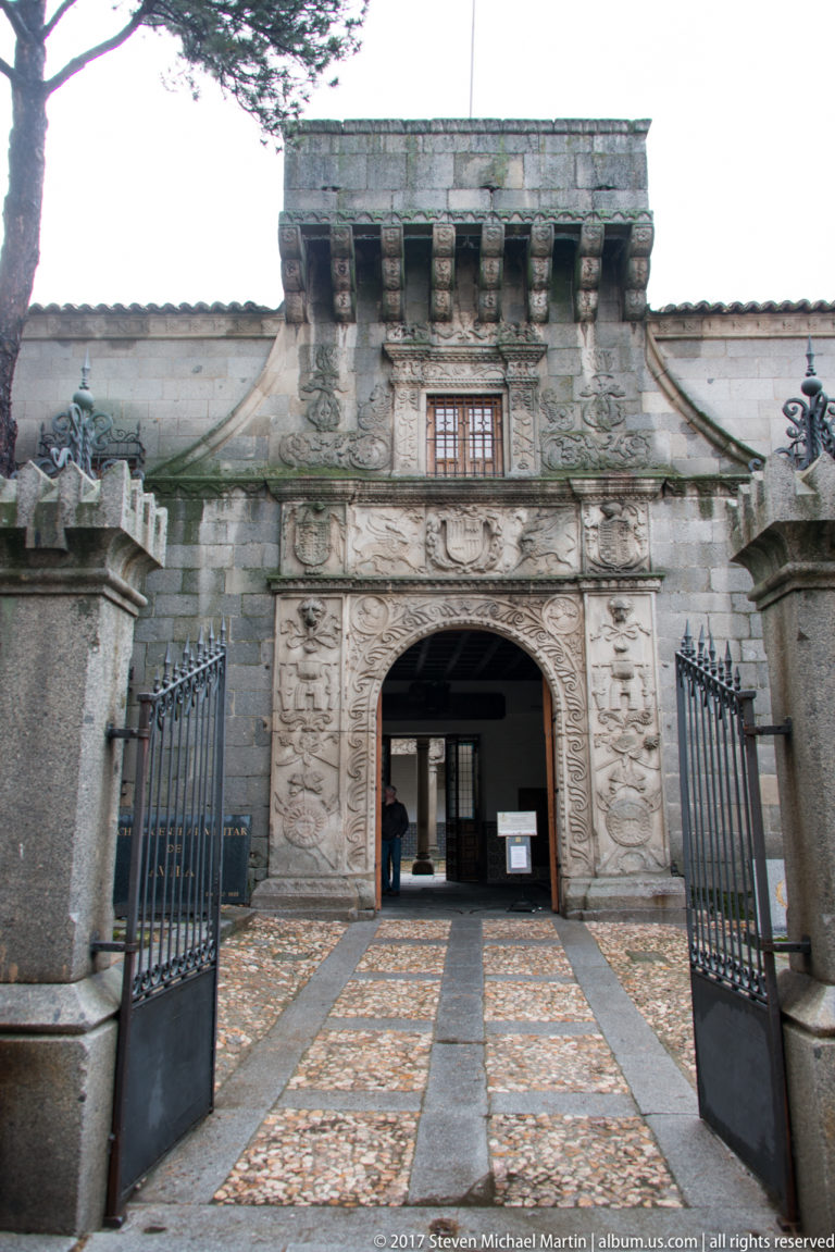 Carved stone entrance with open iron gates, bracketed cornice and pebble-paved approach.