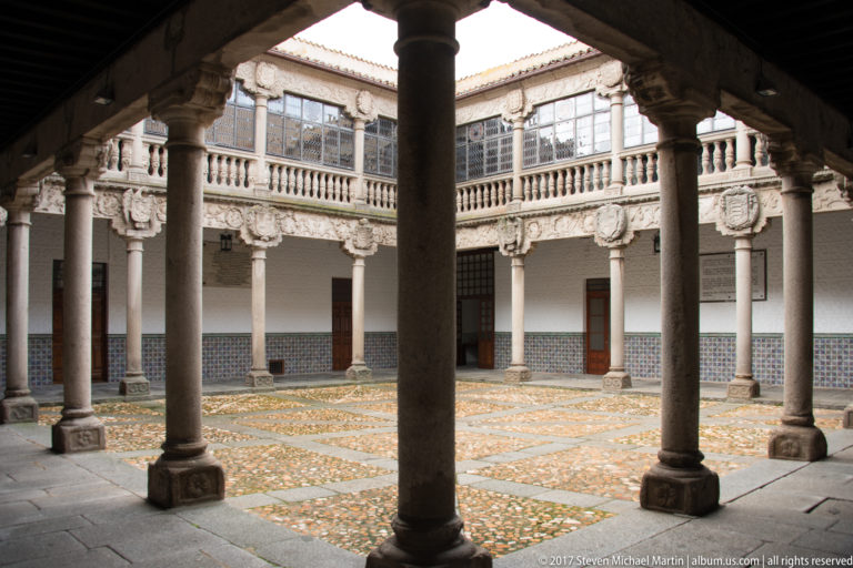 Two-story arcaded courtyard with stone columns, carved shields, balustrades and geometric pebble paving.