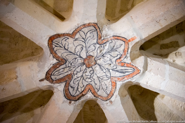 Flower-shaped painted boss with red outline and dark foliate design at the intersection of pale stone vault ribs.