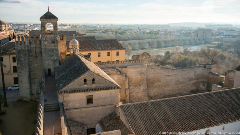 Alcázar towers and roofs in the foreground with the Roman Bridge crossing the Guadalquivir in the hazy distance.