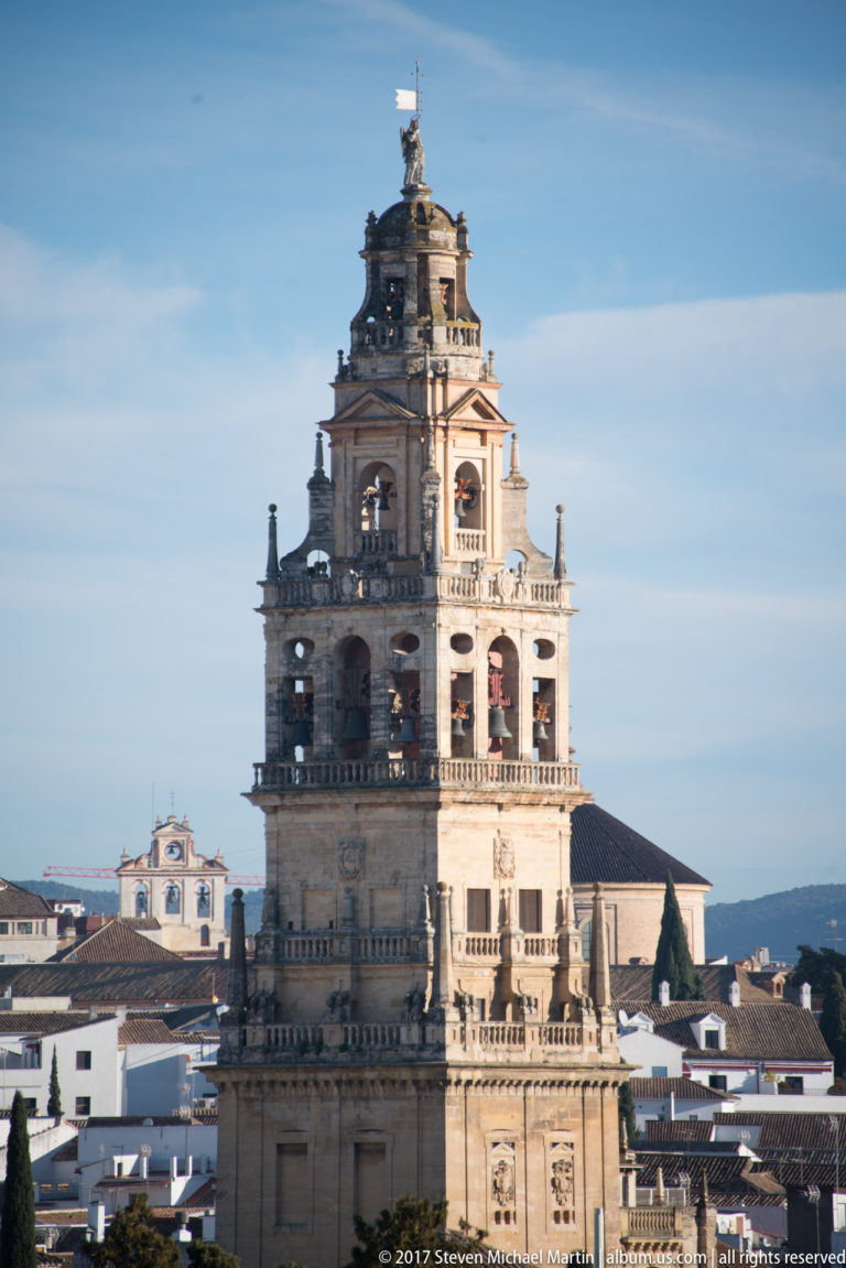 Daytime view of the Mosque-Cathedral bell tower rising above Córdoba’s white rooftops against a blue sky.