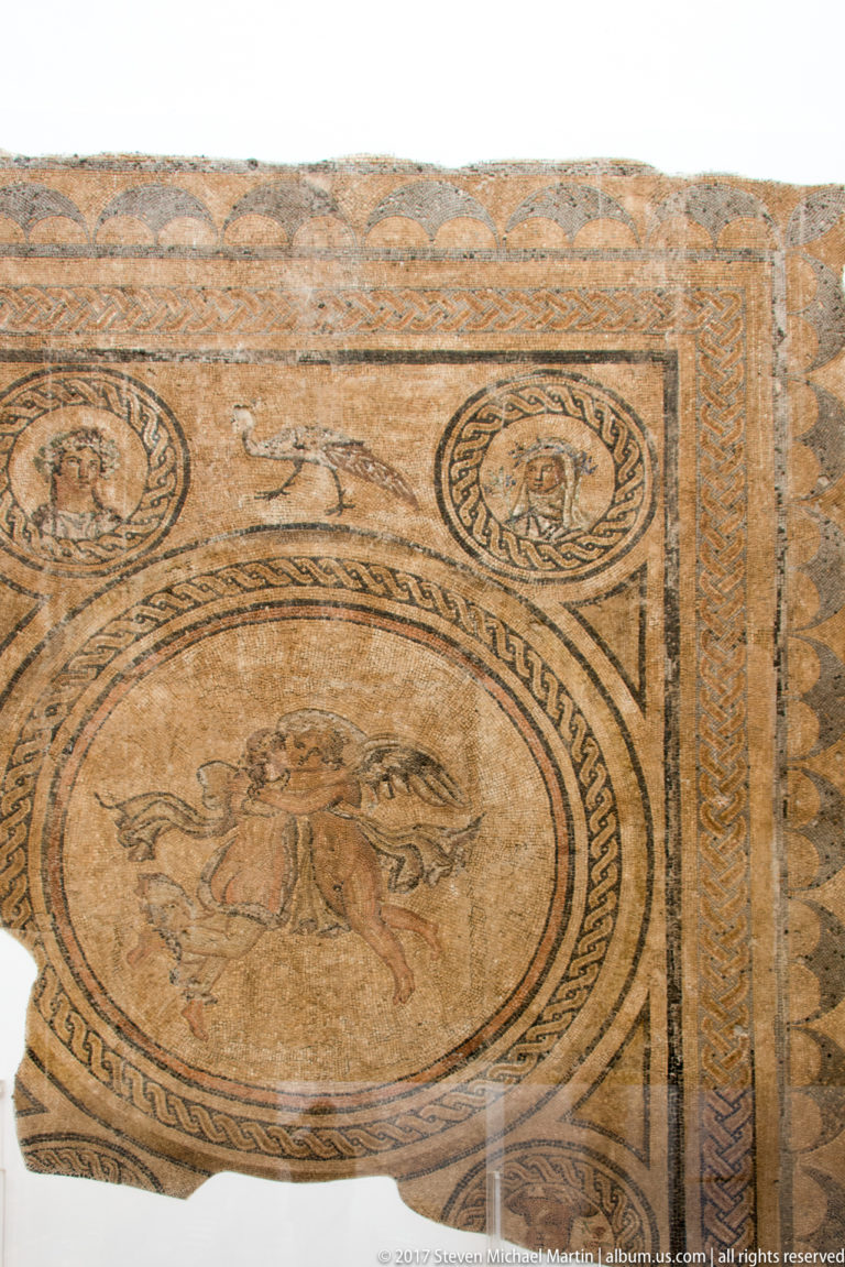 Roman mosaic with a large central figurative medallion, smaller portrait roundels, and braided geometric borders.